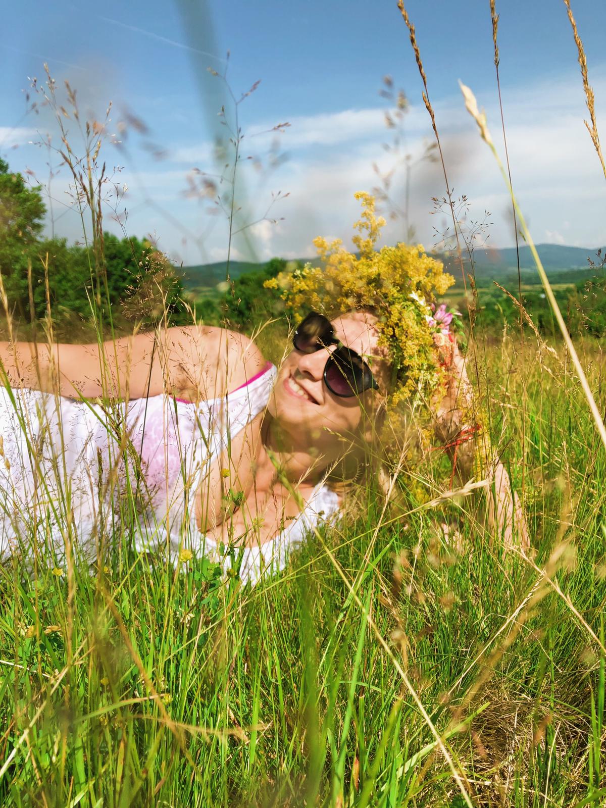 Aminta Georgescu lying in tall summer grass wearing a wreath of wild yellow flowers